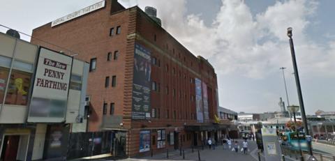 Exterior of Liverpool's Royal Court theatre, a red brick building with large poster advertising performances on the front 