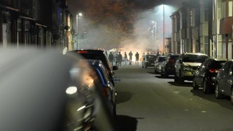 People gather around a fire on a street in Harehills