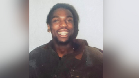 Young man smiling and happy wearing a dark jumper and standing against a white backdrop.