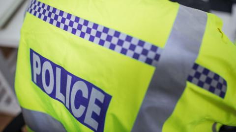 A police officer's fluorescent uniform, with a male officer's back to the camera.