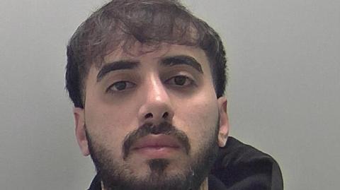 Mugshot of Mohammed, who is wearing a black hoodie and has short black hair, a moustager and a beard