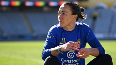 Lucy Bronze in Chelsea kit sitting down on a football pitch