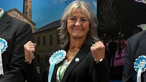 A woman smiles at the camera as she clenches both her fists.