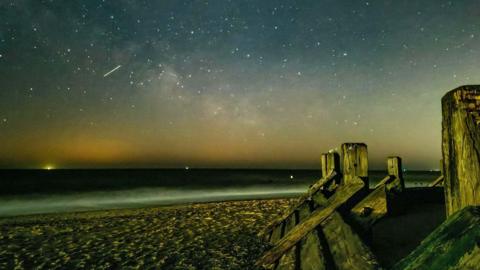 A small meteor streak in a starry sky above the sea, seen from a beach