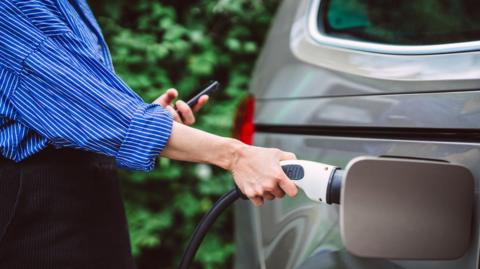 A close-up of a young woman charging her electric car.