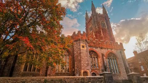 The exterior of the church in an autumn light with a tree on the left