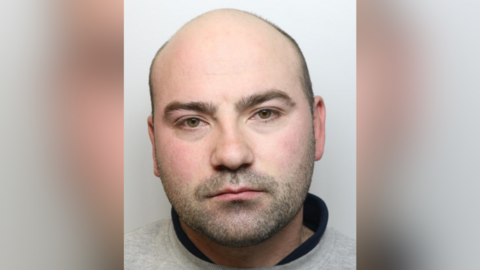 A police mug shot of Russel Thornton who is a white man with very short hair and beard stubble.