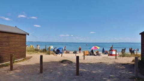 Blue sea under blue sky with the beach in the foreground and people sitting under an umbrella 