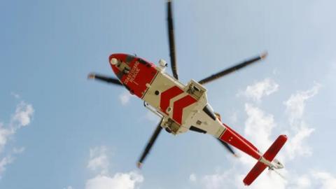 View from below of a red and white HM Coastguard helicopter