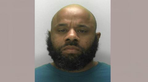 Simeon Bernard is looking at the camera in a police mugshot. He has a bald head and a thick beard.