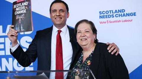 Two people, man and woman, at podium holding up a political manifesto