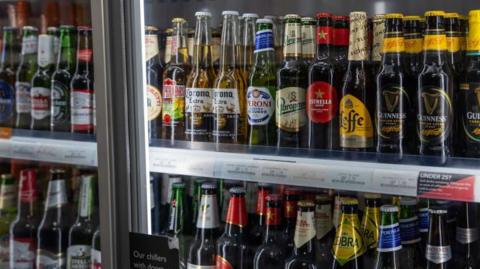 Bottles of various brands of alcoholic drinks on display in a cabinet inside a shop 