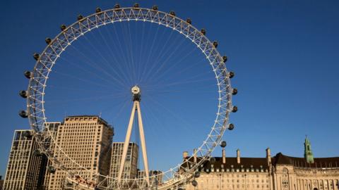 The London Eye ferris wheel against a blue sky with other smaller buildings in the background