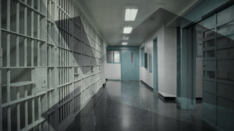 A generic image of a prison. It is a dark room with blue doors and cells to one side.