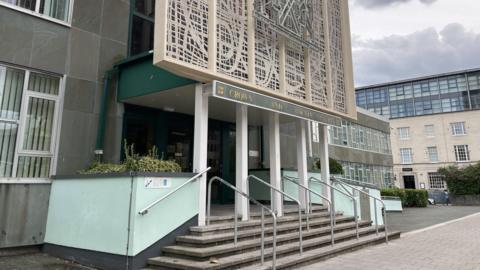 A picture taken from the left side of Plymouth Crown Court looking over to the entrance. It is a large entrance with steps and railings.