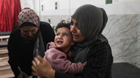 A woman cries as she holds her injured child, who is also crying, in a hospital in Nuseirat, Gaza Strip.