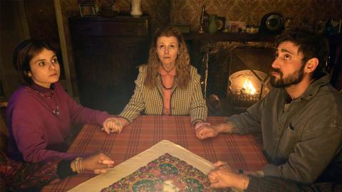Liz (Gabrielle Creevy), Bethan (Sian Gibson) and Bill (Michael SochaI) sit holding hands around a table in a darkened room.