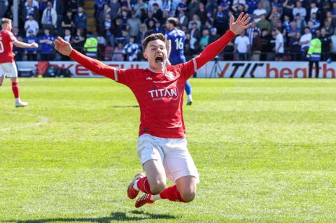 A footballer in a red kit celebrates in a knee slide