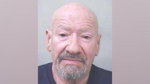 Mugshot showing a old, bald man with a greying goatee beard. He is wearing a navy t-shirt.