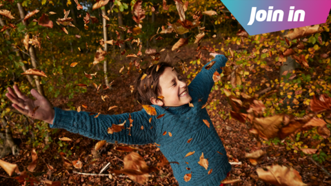 Child smiling and throwing autumn leaves in the air.