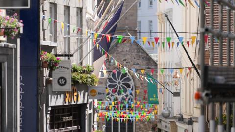 St Peter Port highstreet showing the shops and flags hanging between the buildings 