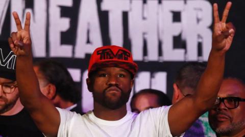 Floyd Mayweather raises his hands in the air during a weigh-in