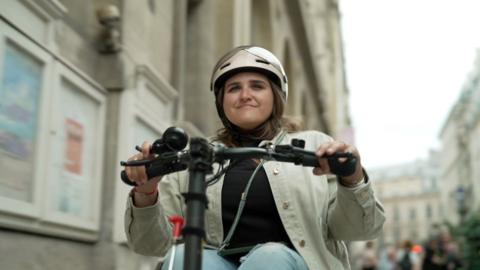 A lady in a shiny helmet rides a disability scooter on a Paris street