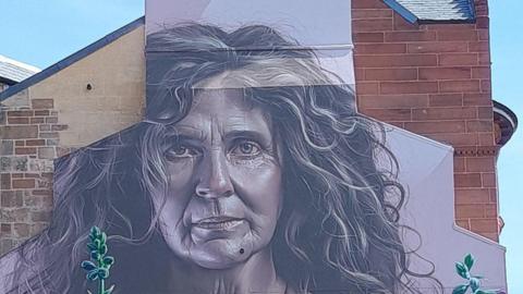 A mural of a woman, painted on the wall of a city building