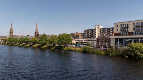 The River Ness flows through Inverness. There are two spires on the bank. 