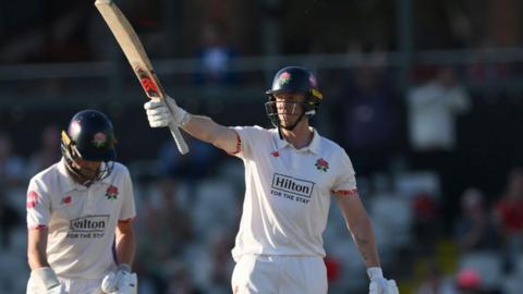 Luke Wells raises his bat after reaching his half-century