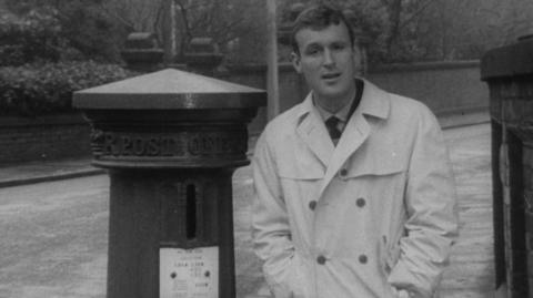 A presenter next to a pillar box.