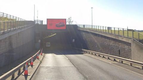 Two lanes lead into a tunnel entrance, there are orange traffic cones along the ourtside edge of the left hand lane