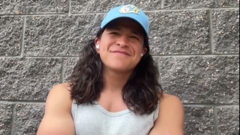 Cristo Fernandez wearing a blue cap and grey singlet leaning against a stone wall.