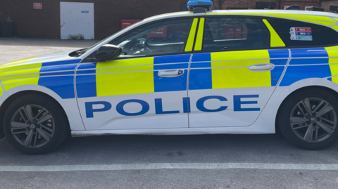 The side view of a police car, with blue and yellow livery, and blue lights on the top