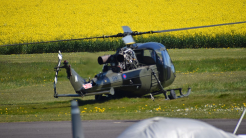A helicopter is parked on green grass with a damaged tail