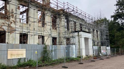 The facade of a mansion house, burnt, and surrounding by scaffolding.