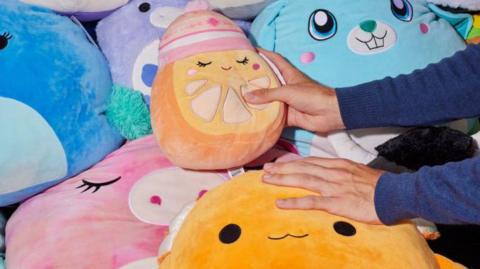 A pile of Squishmallows with one being held in a hand.