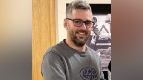 Craig Hurcombe is wearing glasses, has short greying hair and has facial hair. He is smiling at the camera.