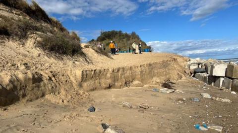 Sandy dunes with sheer drop, with concrete defences to right.