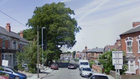 Springfield Road in Kings Heath with houses on both sides, parked cars and lampposts and a roundabout further along the road near a large tree.