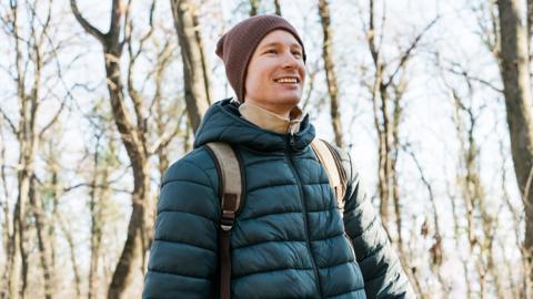 A smiling man, outdoors, wearing a backpack, walking in the forest, autumn weather.