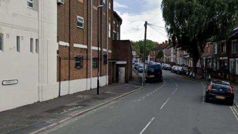 A Google street view showing the Edmund Rd street sign. The street has a large temple building on the left and rows of terraced houses on the right. Parked cars line both sides of the road.