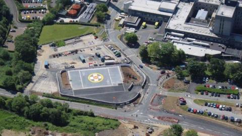 An aerial view of the helipad with a white cross in the middle with a yellow circle around it 