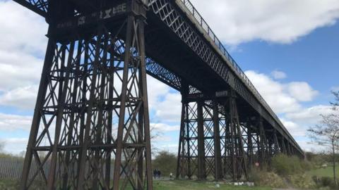 A view of Bennerley Viaduct, near Ilkeston, from underneath it with people walking below it in the distance.