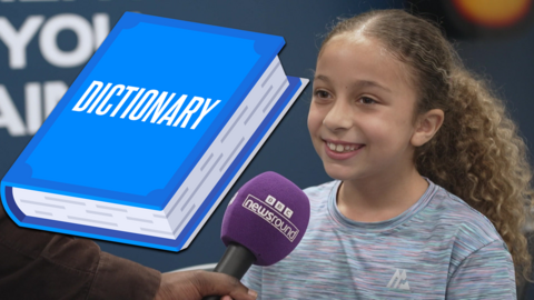 A blue dictionary and a girl smiling while speaking into a microphone. 