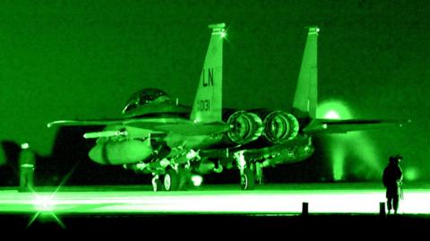 The rear of a USAF F-15 fighter jet photographed at night, in a green night-sight hue