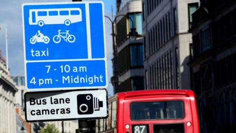 An image of a bus lane sign showing what times you can access the lane. Underneath, another sign reads bus lane cameras.