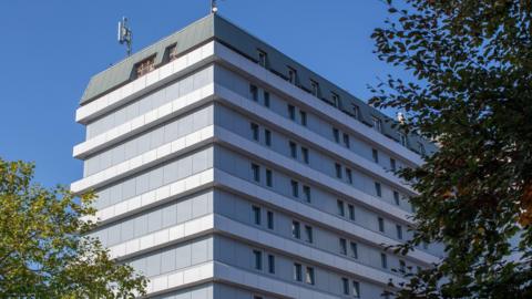 An external view of the Gloucestershire Royal Hospital tower block with some trees in the foreground