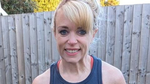 Loretta Davies has bright blonde hair tied back with a sweeping side fringe, and smiles towards the camera. 