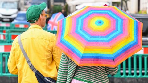 A woman carries a colourful umbrella during a rain shower near Pall Mall on August 20, 2026 in London, England.
